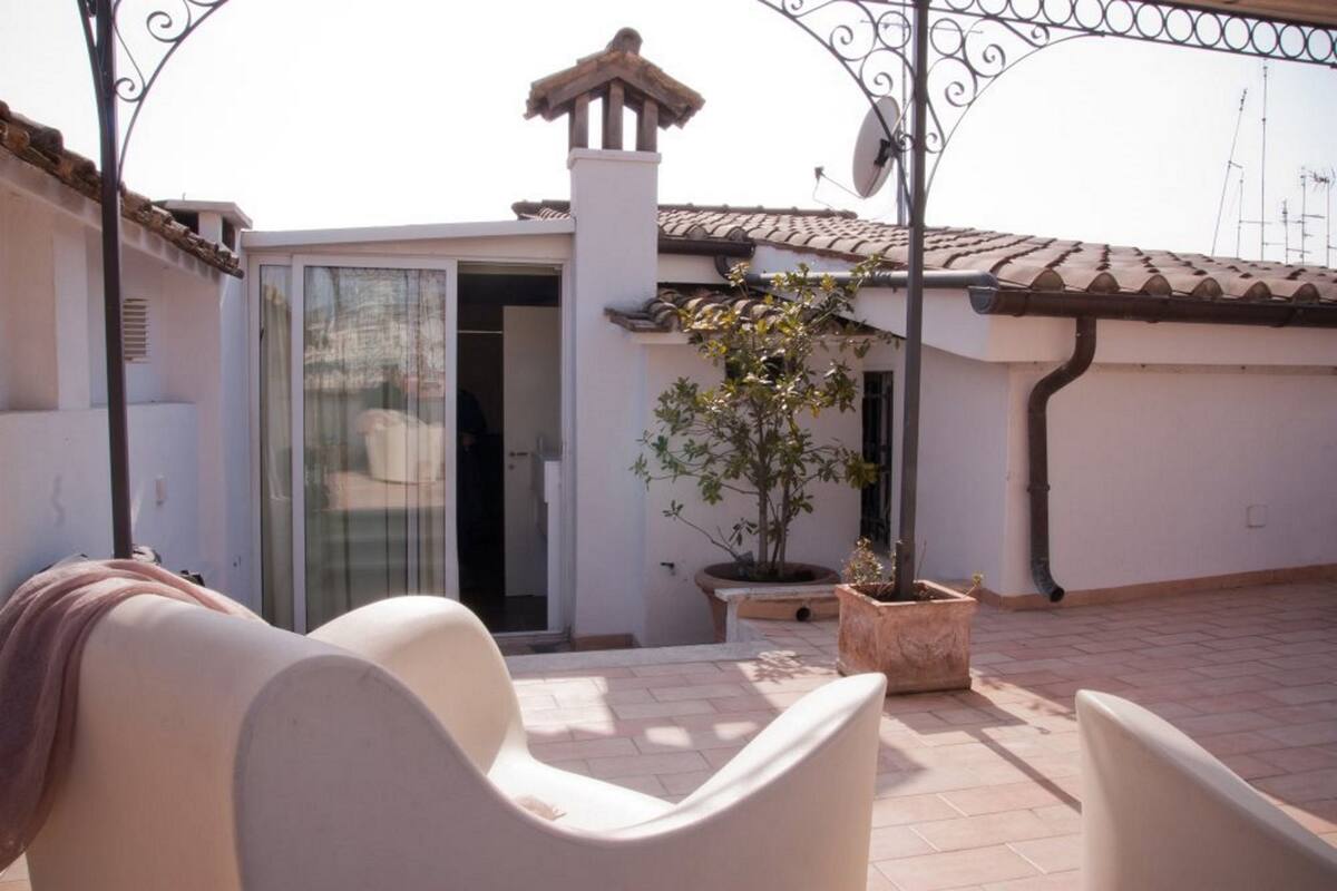 A patio with two white chairs, a potted plant, and a glass door leading to a room.