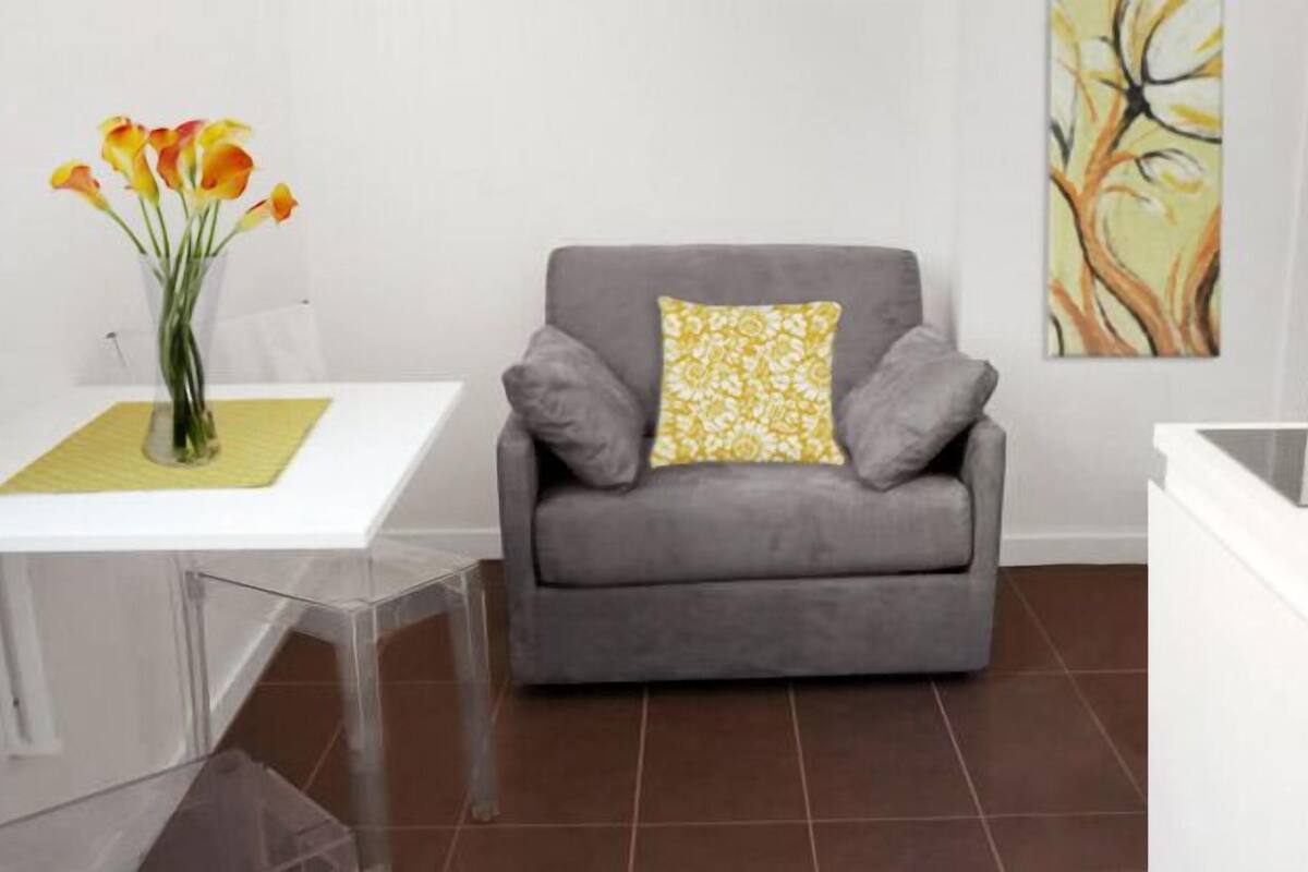A modern living room with a grey sofa, a clear glass table, a vase with flowers, and a painting on the wall.