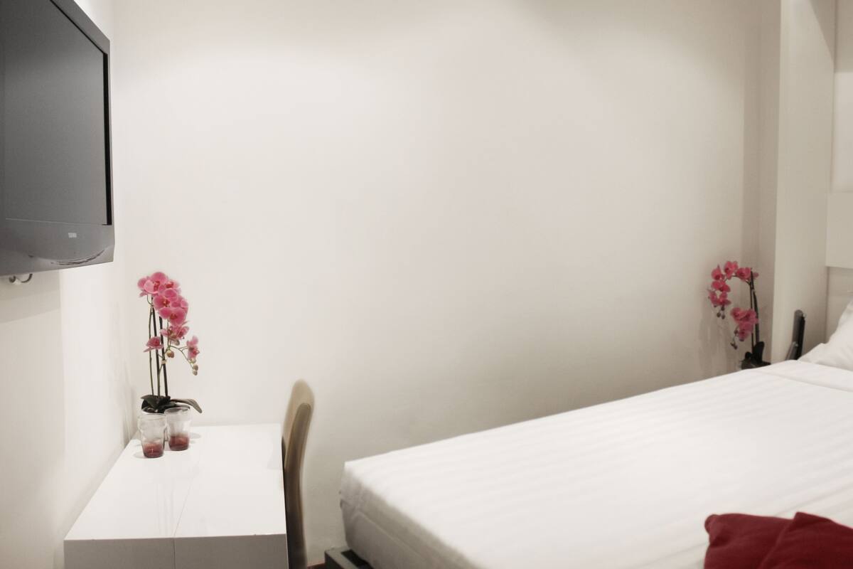 A hotel room with a bed, a desk, a chair, and two pink orchids on the wall.