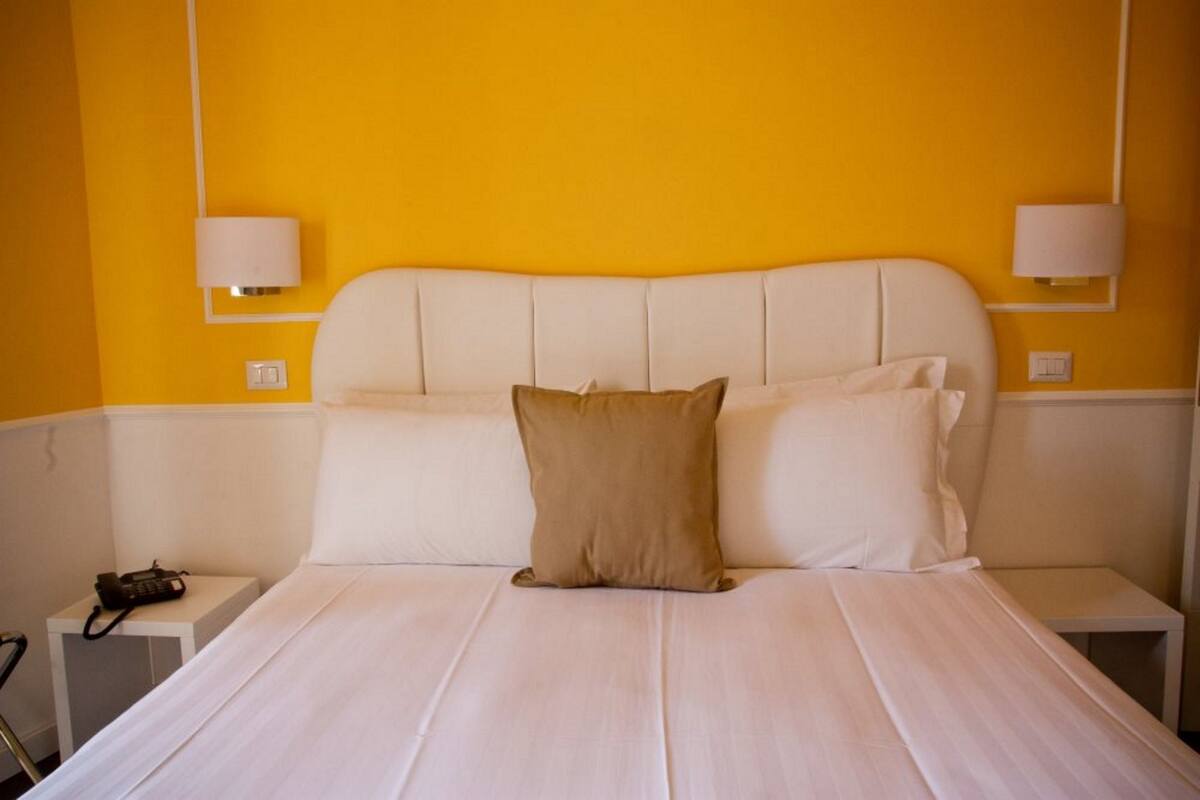 A bed with white bedding and two pillows, a bedside table with a lamp, and a phone on the side table.