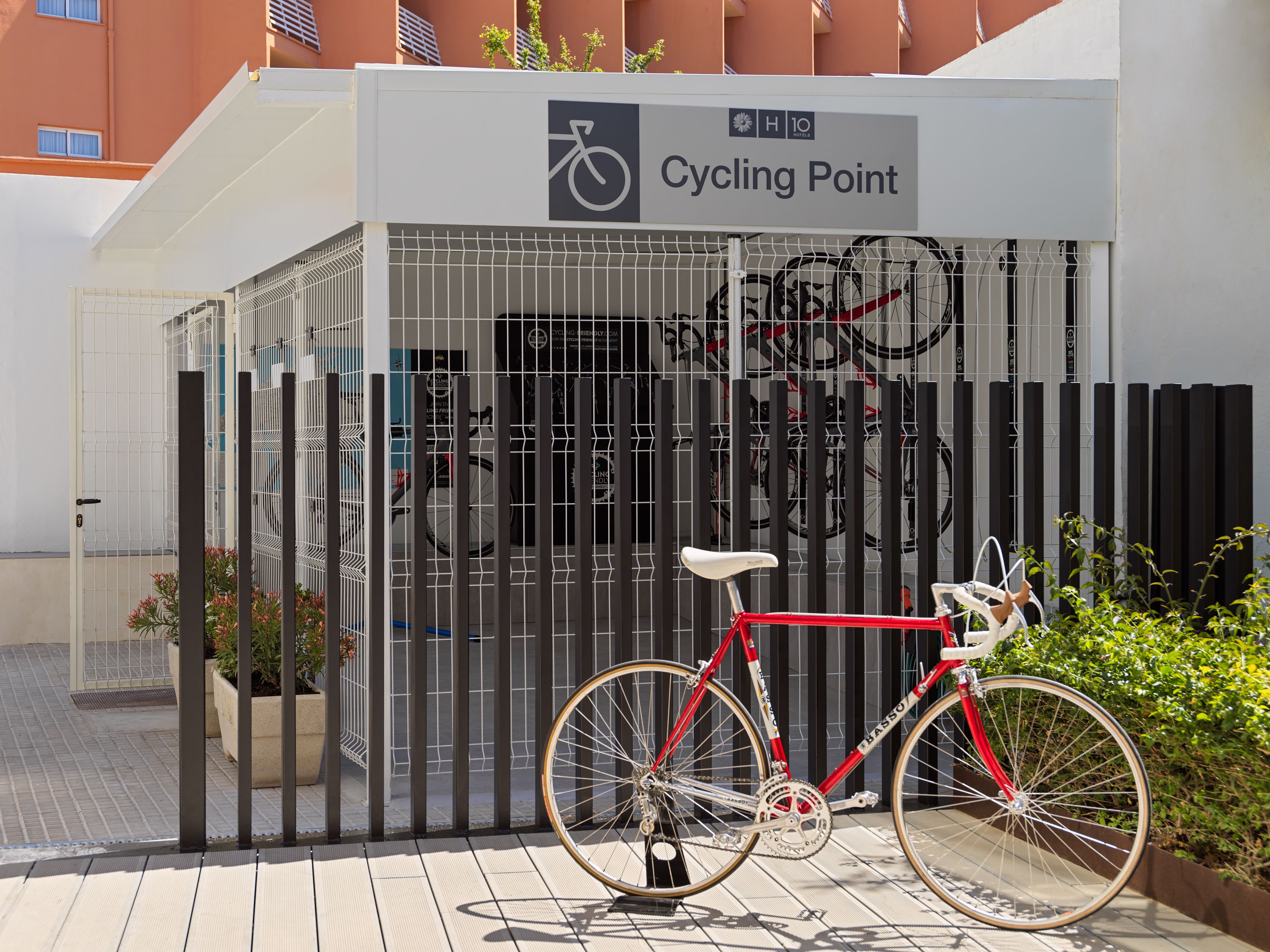 Entrada de hotel con señal de punto de ciclismo, una bicicleta roja y una valla de metal.