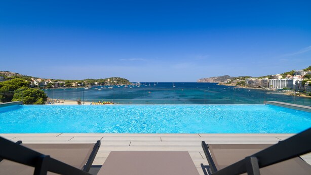A pool with clear blue water, surrounded by lounge chairs and a view of the sea and buildings. - H10 Casa del Mar (Calvia)