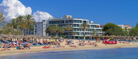 A beach resort with multiple levels of balconies, palm trees, and beach umbrellas.