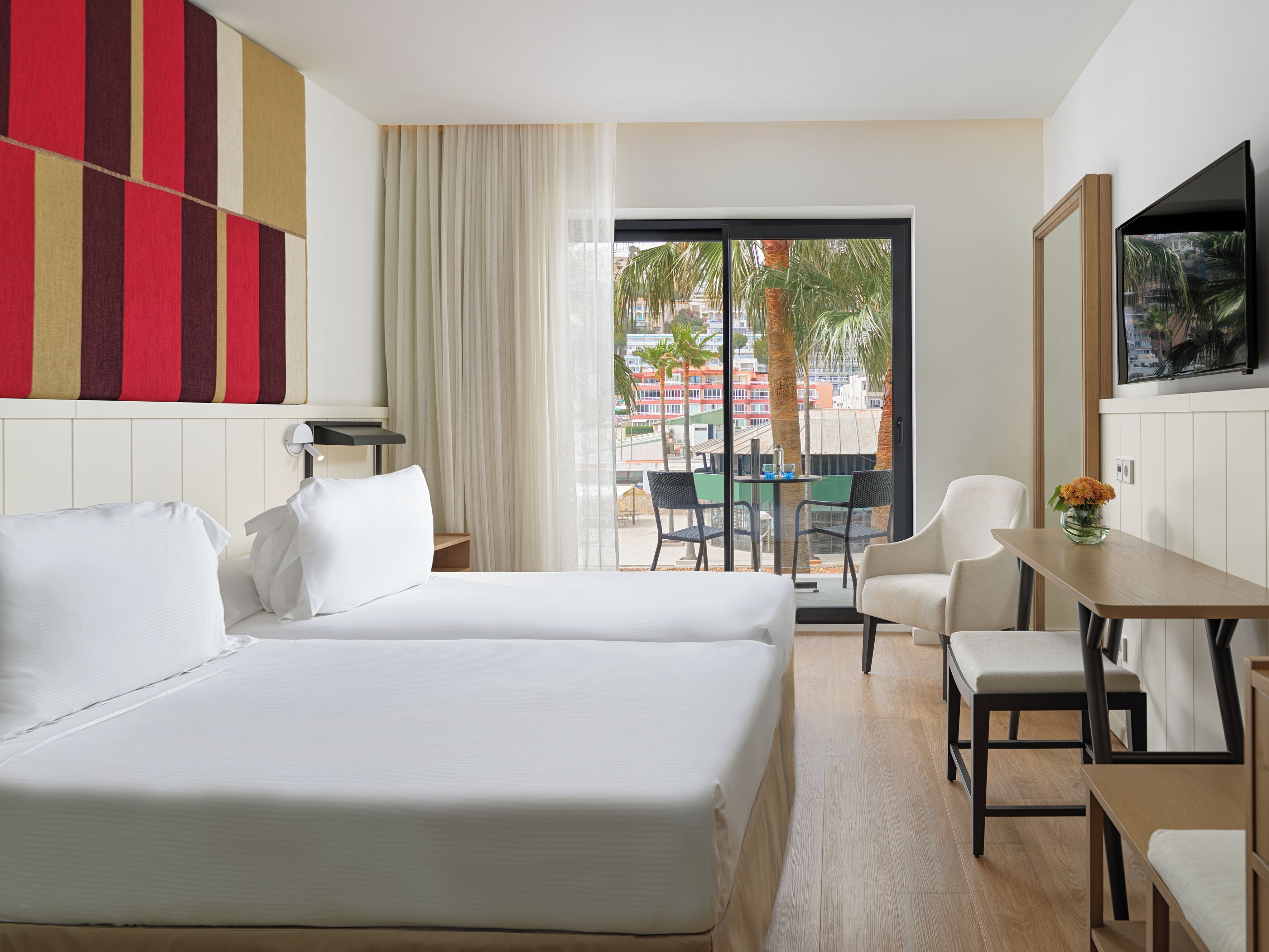 A hotel room with two beds, a dining area, and a view of the cityscape.