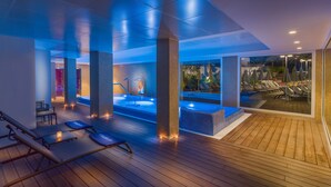 A modern indoor pool area with a wooden deck, lounge chairs, and a hot tub. - H10 Casa del Mar (Calvia)