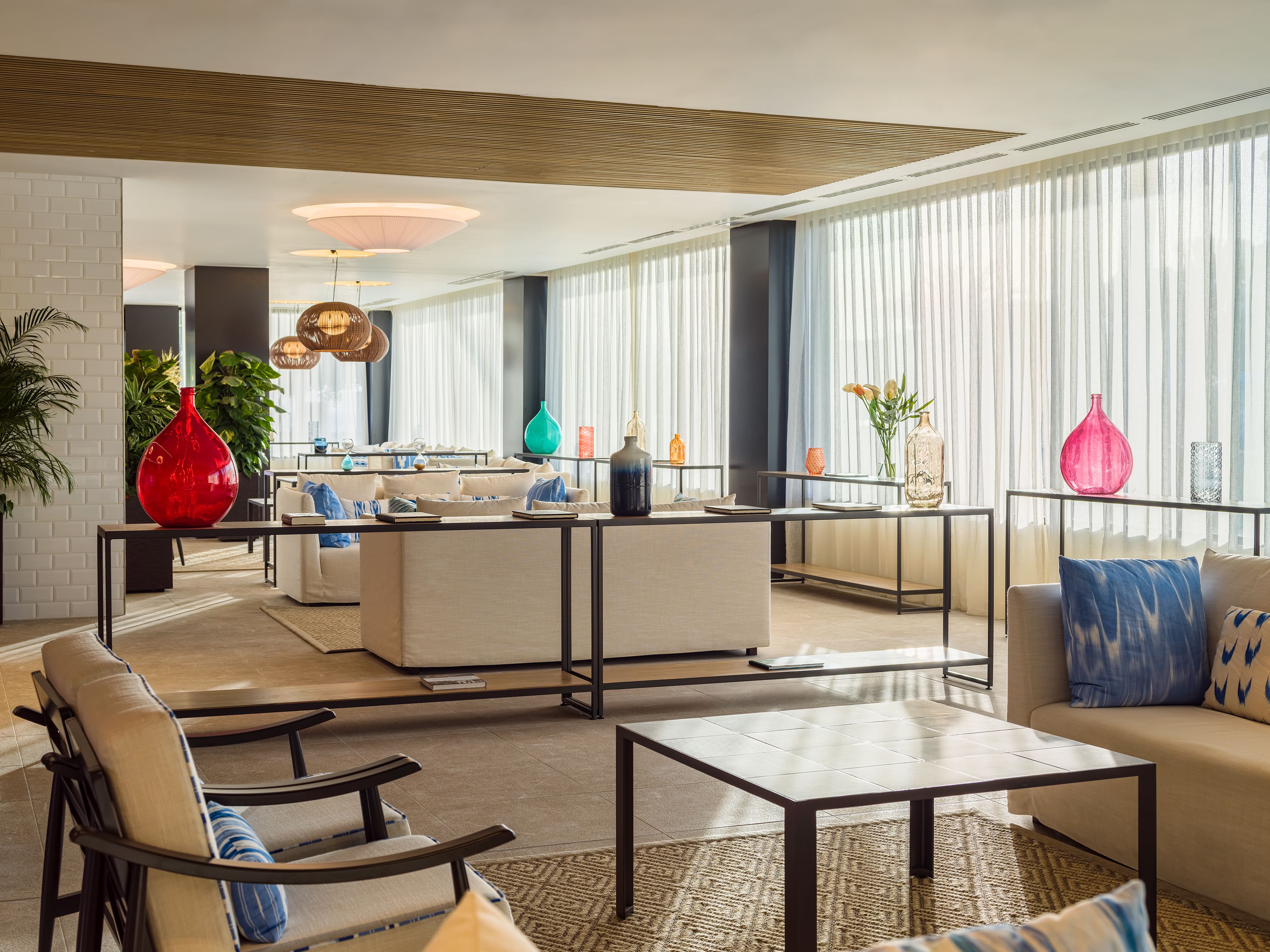 A modern hotel lobby with a central seating area, large windows, and various decorative vases.