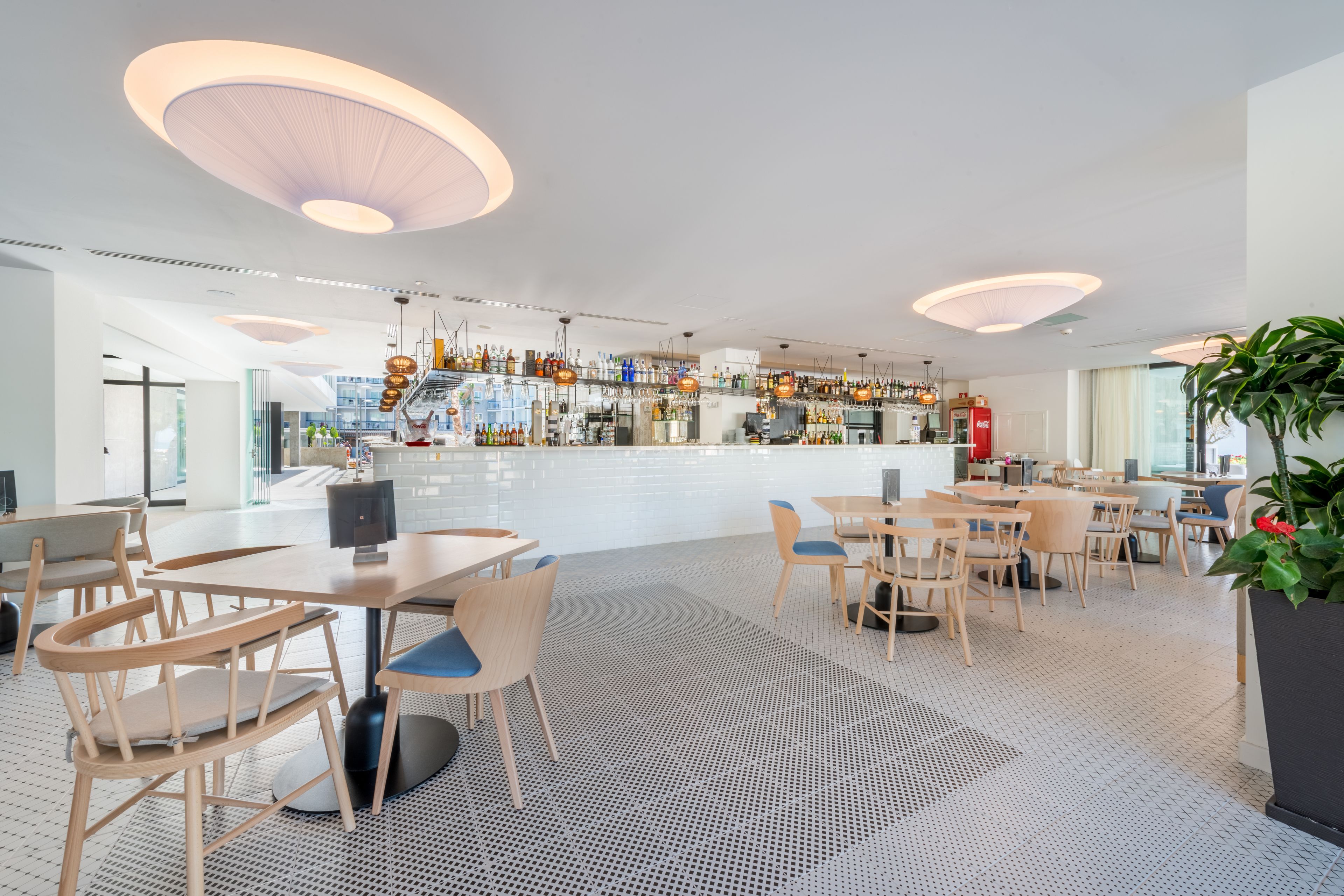 A modern restaurant with a bar area, wooden tables and chairs, and pendant lighting.
