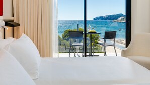 A hotel room with a bed, a table with chairs, and a view of the sea and cliffs. - H10 Casa del Mar (Calvia)