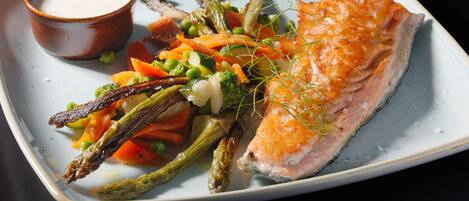 A plate with salmon, asparagus, peas, carrots, and a small bowl of sauce.