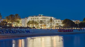 A beachfront hotel with multiple balconies, palm trees, and beach chairs. - H10 Casa del Mar (Calvia)