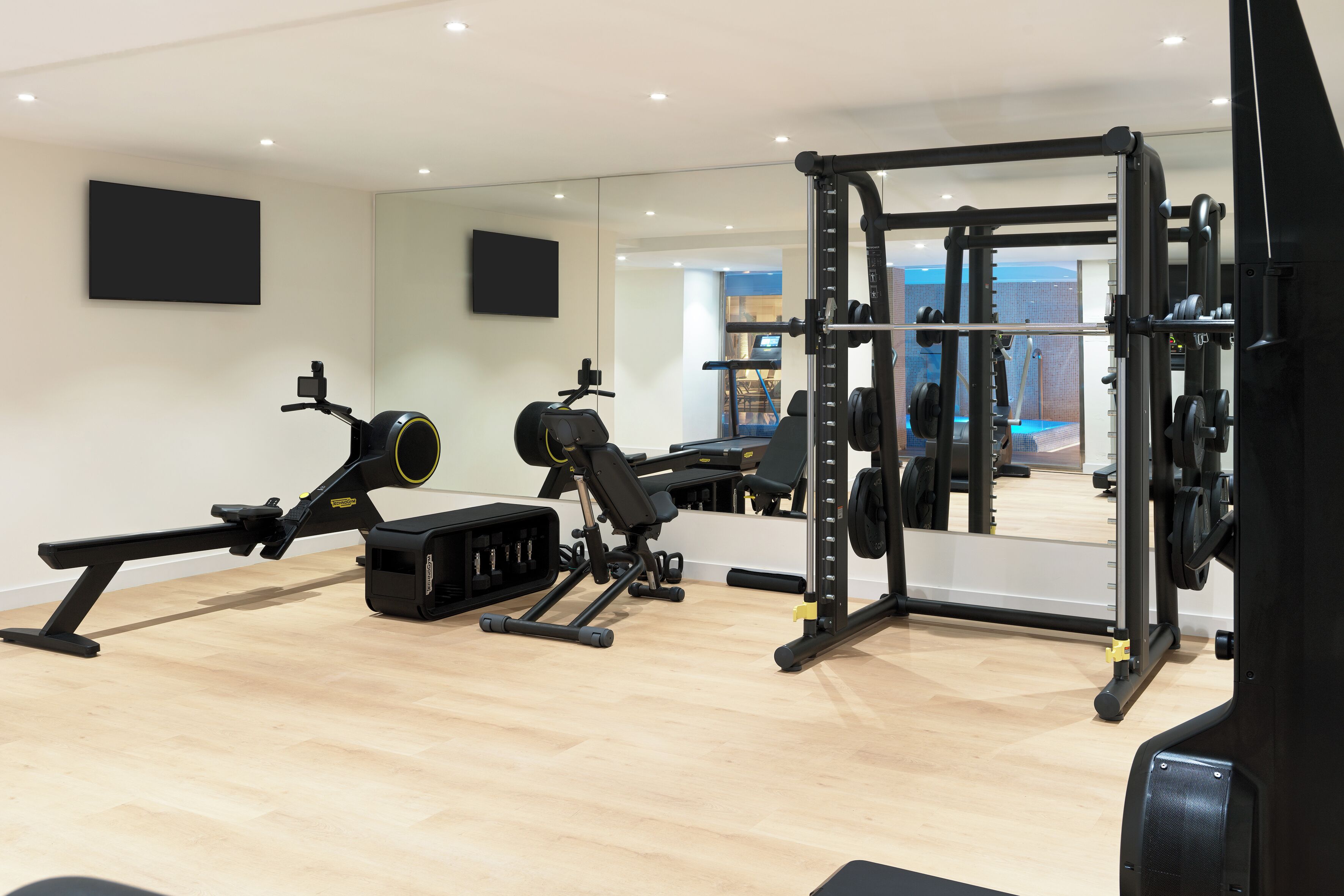 A modern gym with exercise equipment, a large mirror, and a wooden floor.