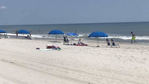 Una playa con sombrillas azules, sillas de playa y algunas personas.