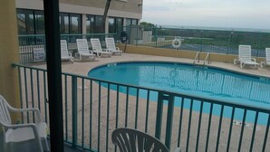 Una piscina con vistas al océano, rodeada de sillas de descanso y un edificio con grandes ventanales.