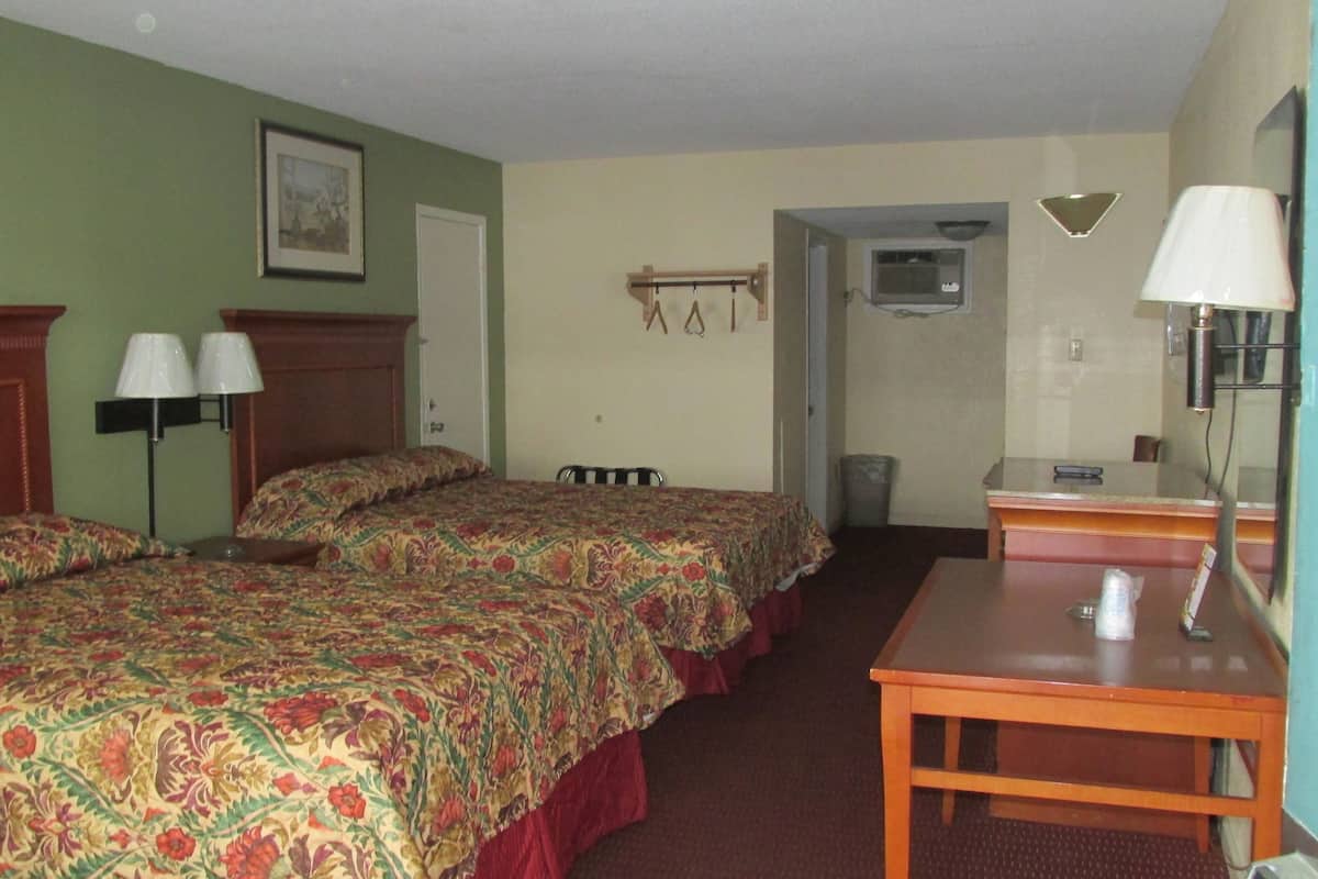 Een hotelkamer met twee bedden, een bureau, een stoel, een lamp, een schilderij aan de muur en een airconditioner.