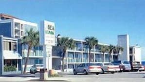 Un hotel moderno con estacionamiento, varios coches y palmeras.