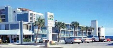 A modern hotel with a parking lot, several cars, and palm trees.