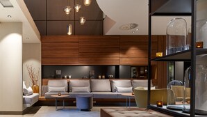 Una sala de estar moderna con un sofá, un reposapiés y una mesa de centro. Hay objetos decorativos en las estanterías y una lámpara en el techo.