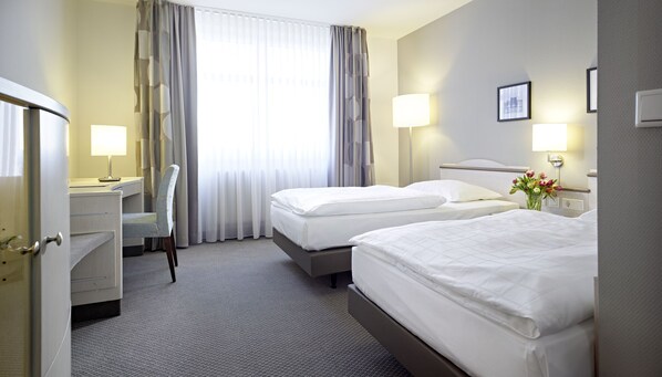 A hotel room with two beds, a desk, a chair, and a window with curtains.