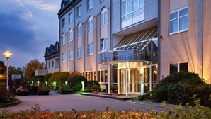 Una entrada de hotel con toldo de cristal, acceso cubierto y un camino de entrada bien iluminado.