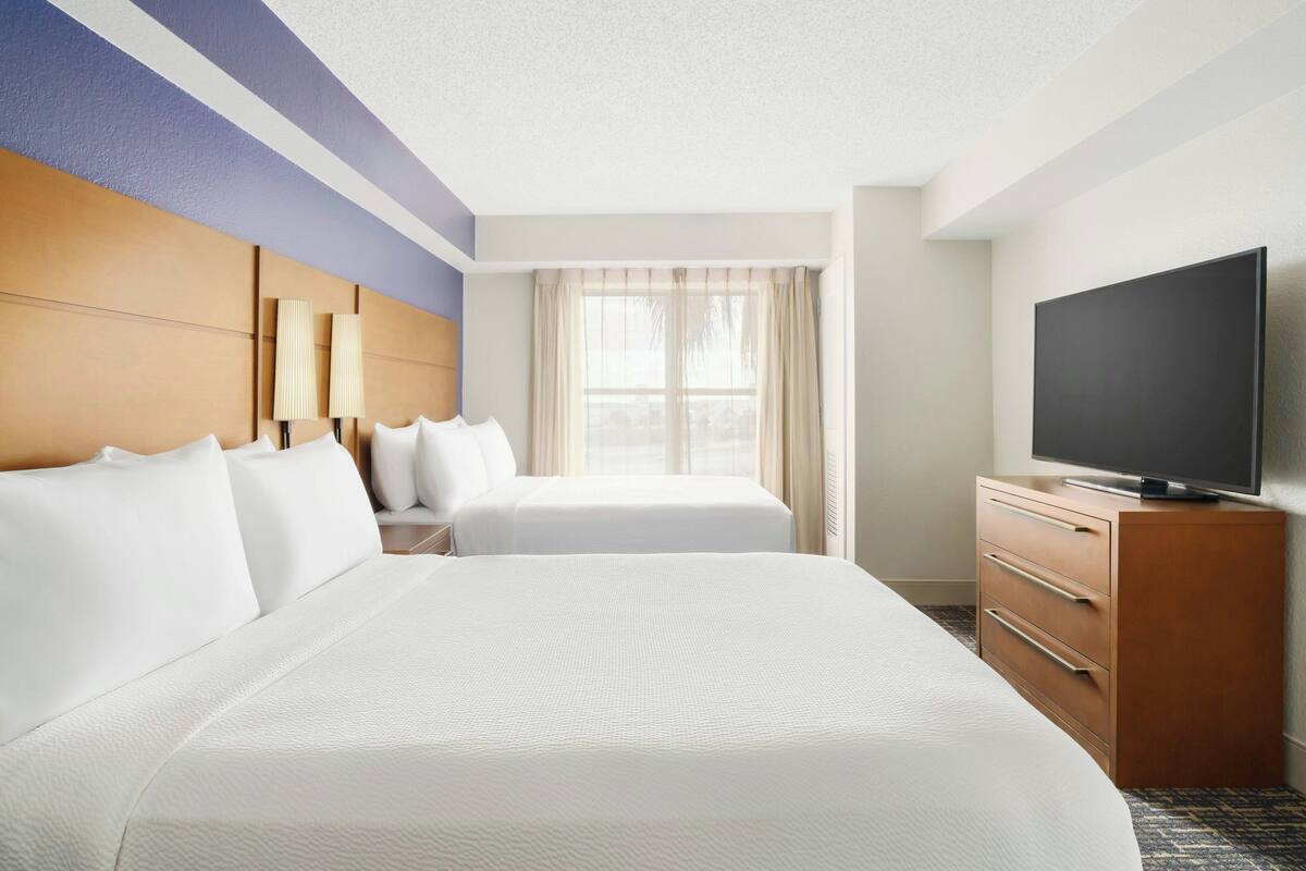 Ein Hotelzimmer mit einem großen Bett, einem Fernseher auf einer Holzkombie und einem Fenster mit Vorhängen.