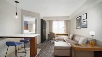 A modern hotel room with a kitchenette, a sofa, a desk, and a chair.