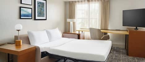 A hotel room with a bed, a desk, a chair, a TV, and framed pictures on the wall.