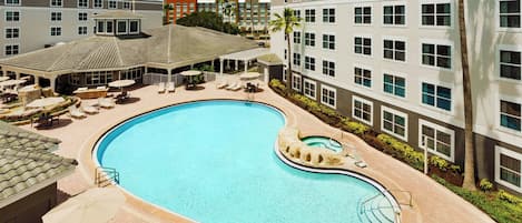 A hotel with a swimming pool, lounge chairs, and a covered patio area.