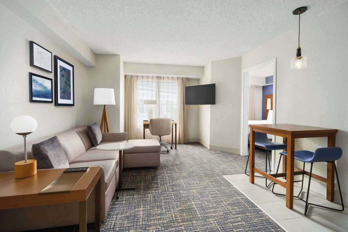 Ein Hotelzimmer mit Sofa, einem kleinen Tisch, einem Fernseher und einem Schreibtisch mit Stühlen.