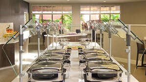 Un buffet avec plusieurs postes de service proposant différents plats et une zone centrale pour la distribution des aliments.