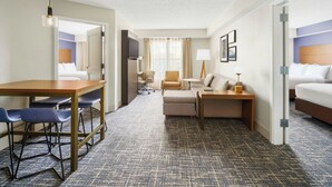 Une chambre d’hôtel avec un bureau en bois, des chaises bleues, un canapé, un lit et un téléviseur.