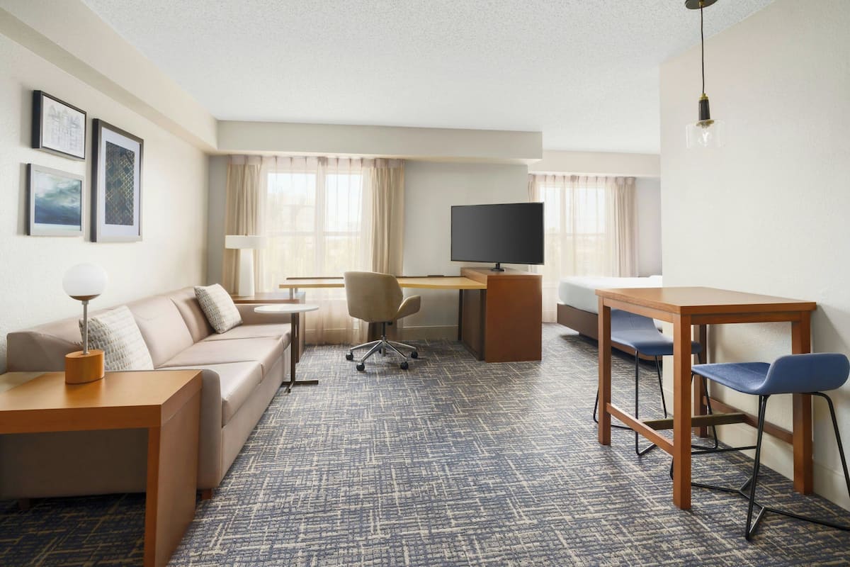 Ein Hotelzimmer mit Sofa, Schreibtisch, Fernseher, Stuhl und Lampe.