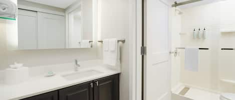 A modern bathroom with a white sink, dark cabinets, a glass shower enclosure, and a large mirror.
