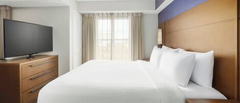 Habitación de hotel con una cama grande, un televisor sobre un aparador de madera y una ventana con cortinas.