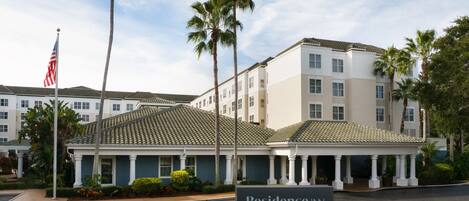 Um hotel com vários andares, entrada coberta e palmeiras.
