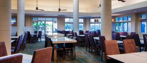 A spacious dining area with high ceilings, large windows, and multiple tables and chairs.