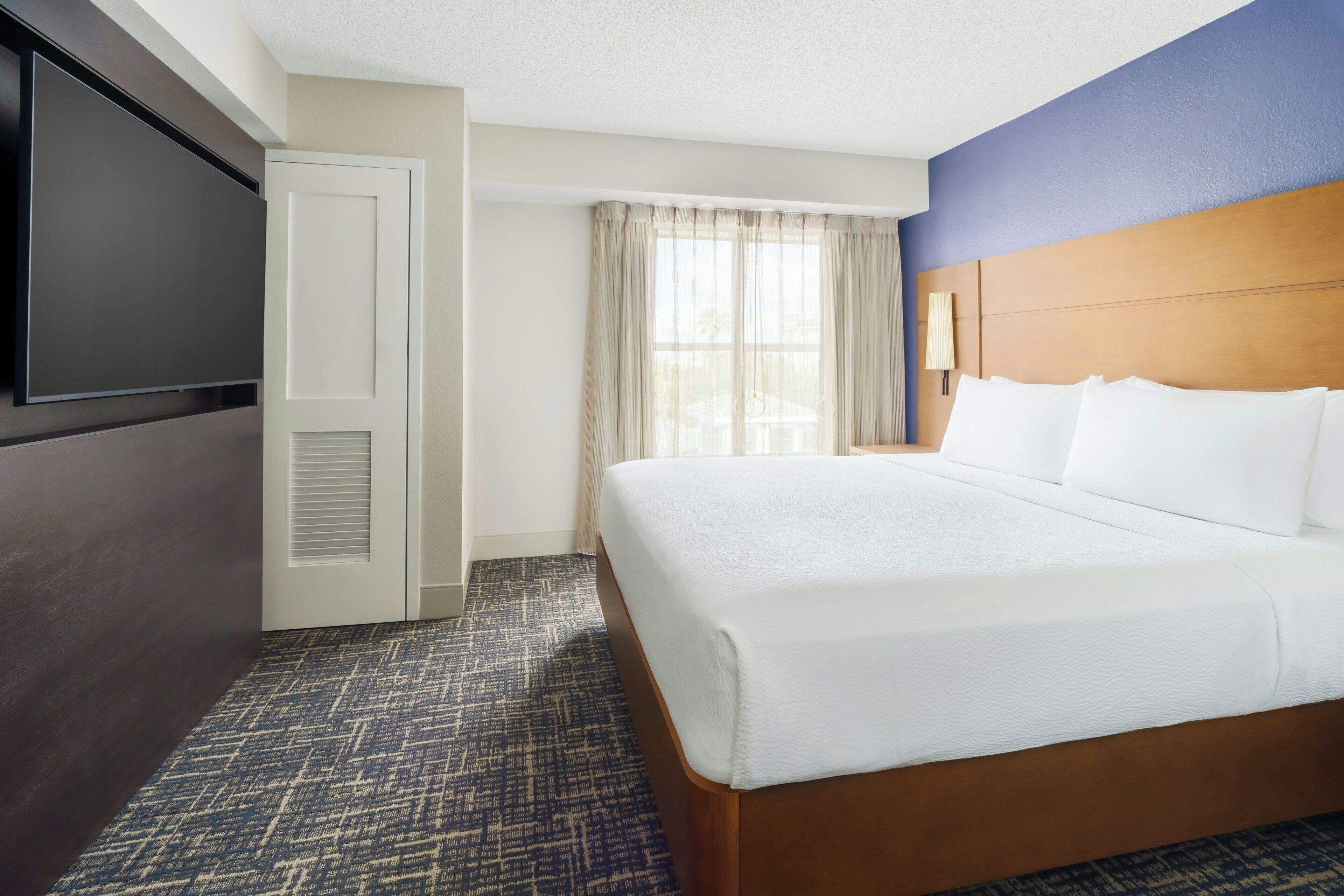 Een hotelkamer met een groot bed, een televisie, een deur en een raam met gordijnen.