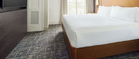 Een hotelkamer met een groot bed, een televisie, een deur en een raam met gordijnen.