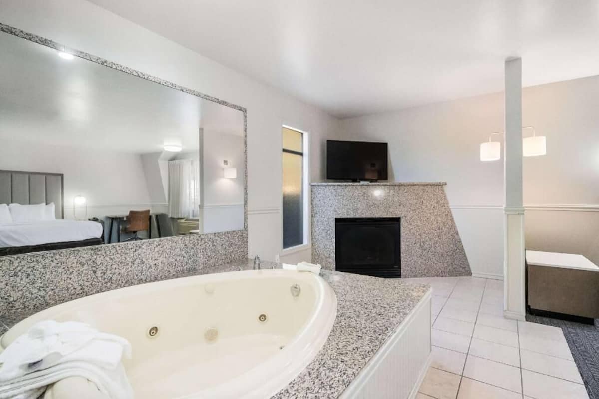 A modern bathroom with a large bathtub, a mirror, a fireplace, and a television.