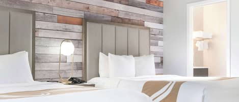 Habitación de hotel con dos camas, un panel de madera, una lámpara de noche y una puerta con perchero.