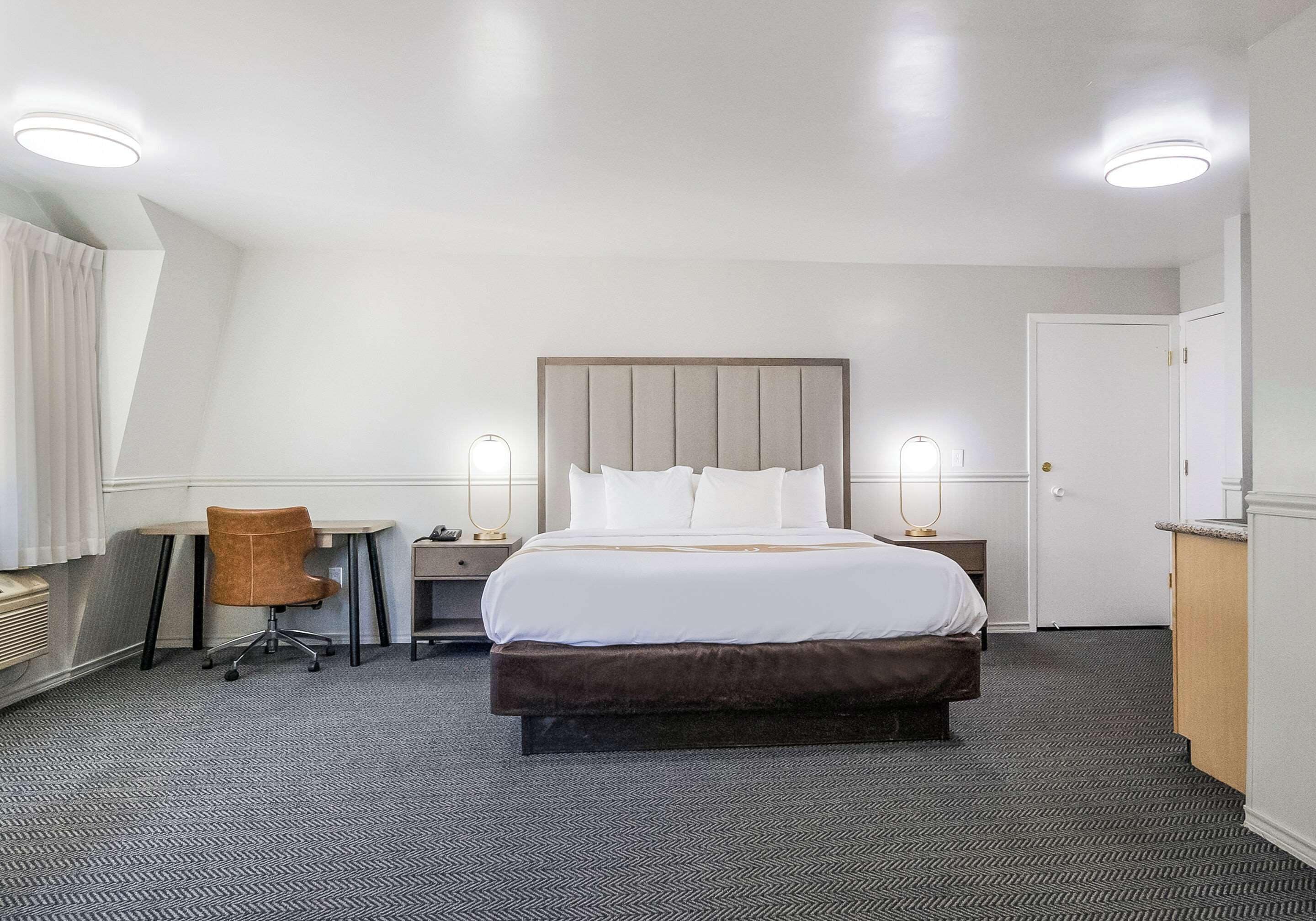 Une chambre d’hôtel avec un grand lit, un bureau, une chaise et une armoire.