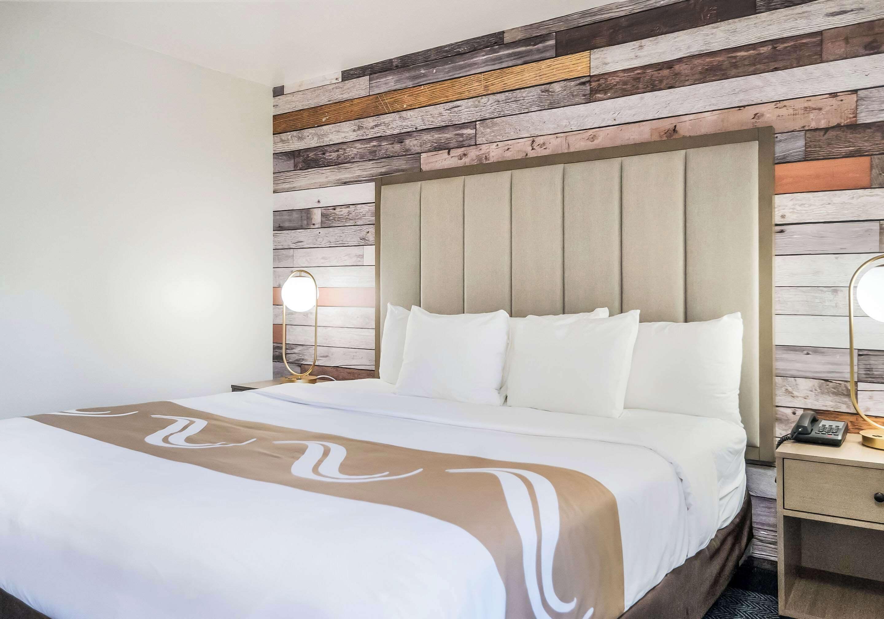Habitación de hotel con cama, mesita de noche y pared decorada con tablones de madera.