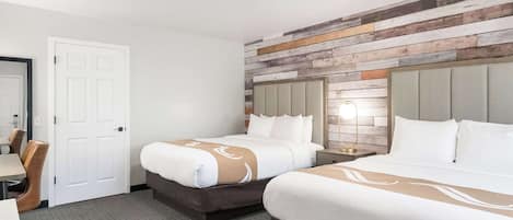 A hotel room with two beds, a desk, and a chair.
