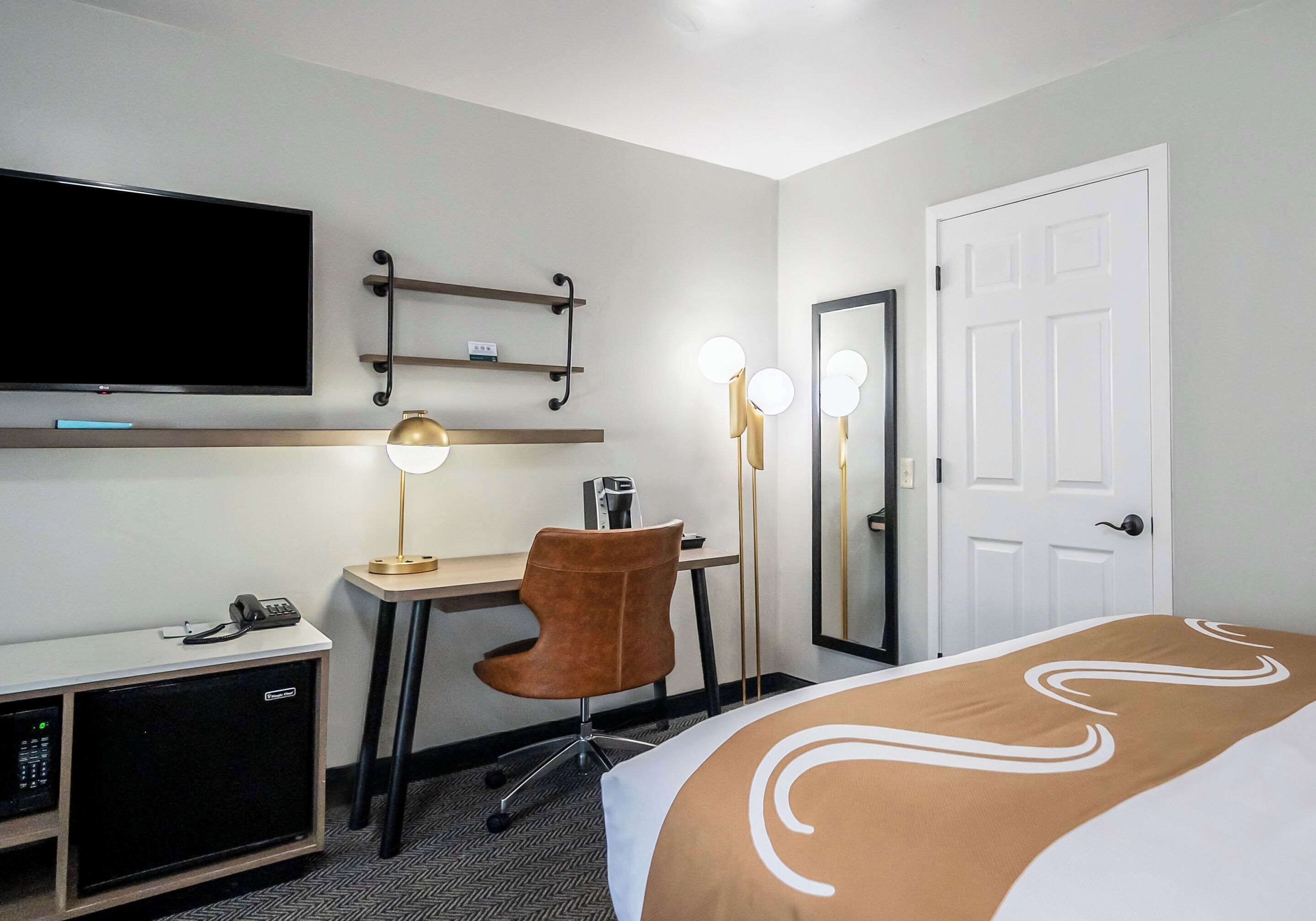 A hotel room with a bed, desk, chair, television, and a minibar.