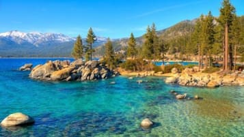 A clear lake surrounded by rocks and trees with mountains in the background.