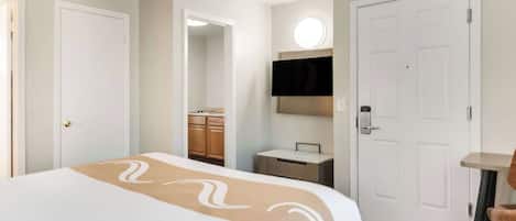 Una habitación de hotel con cama, escritorio, silla, televisor y armario.