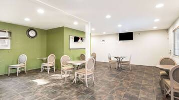 A room with green walls, a clock, a TV, and multiple tables and chairs.