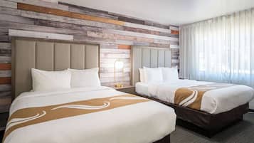 Une chambre d’hôtel avec deux lits, un décor mural en lambris de bois, une grande fenêtre avec des rideaux légers et un sol recouvert de moquette.