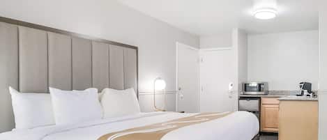 Habitación de hotel con una cama grande, una mesita de noche con lámpara, microondas y una pequeña cocina americana.