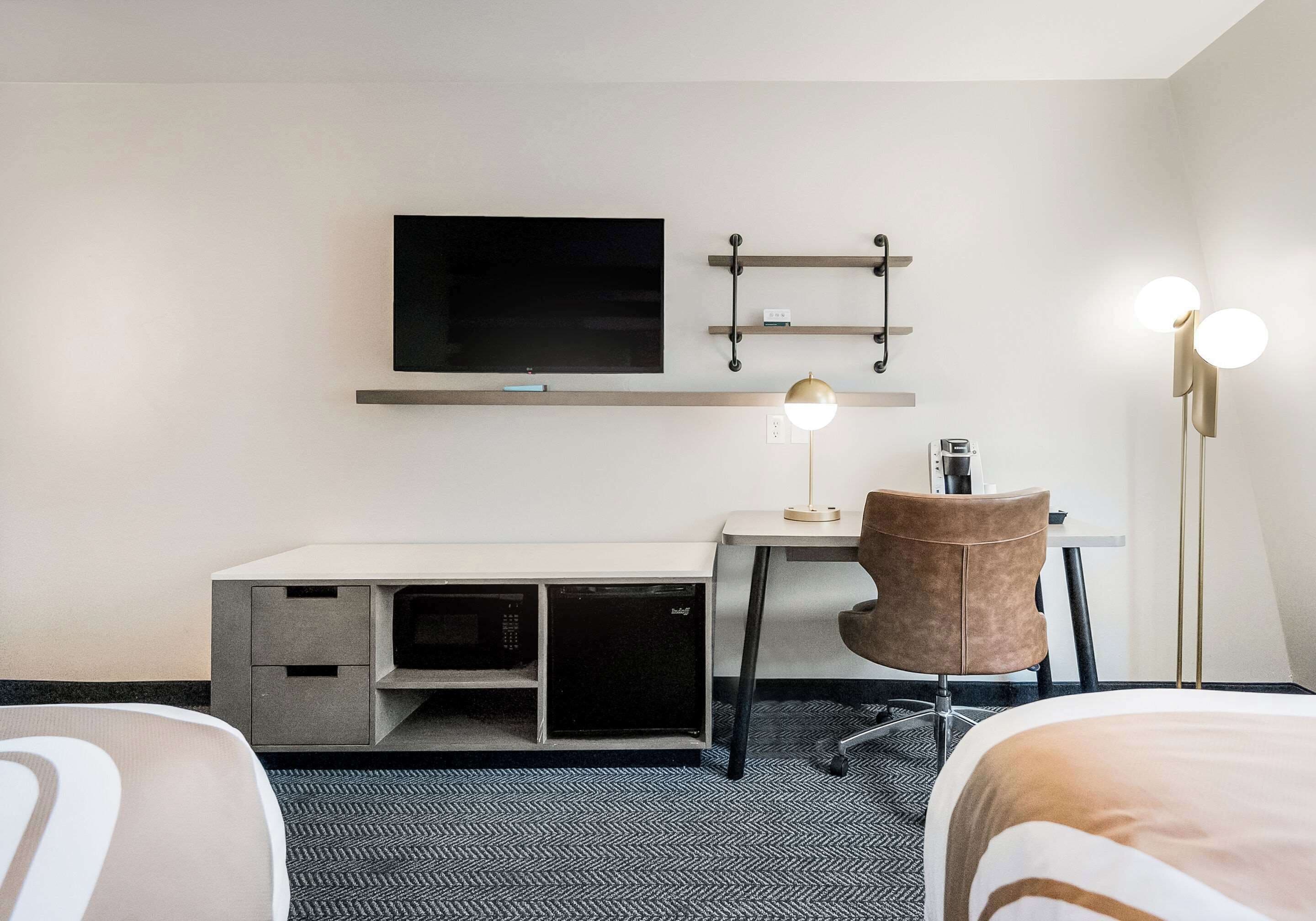 Habitación de hotel con escritorio, silla, televisor y mesitas de noche.