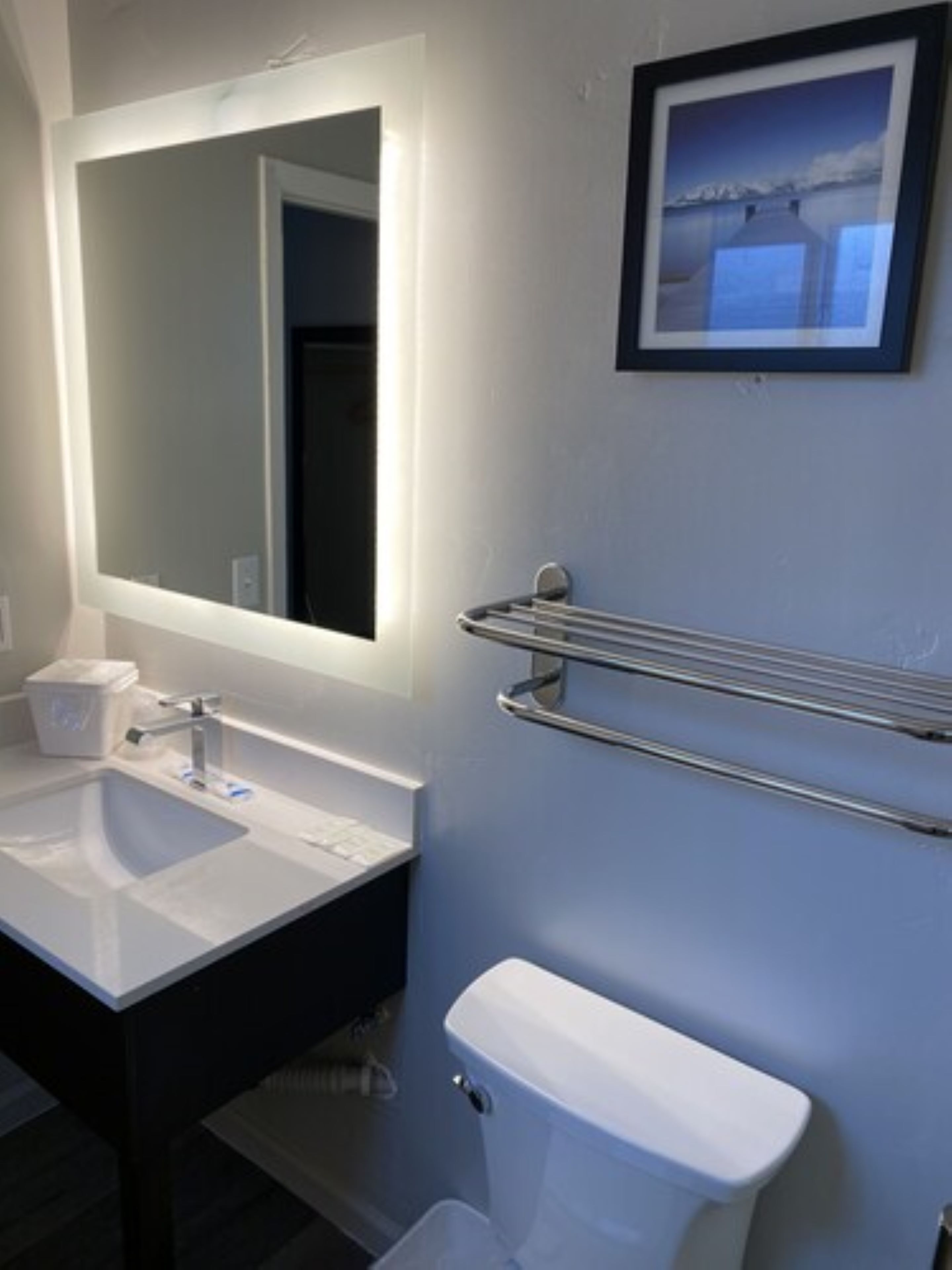 A bathroom with a white sink, a mirror, a toilet, and a towel rack.